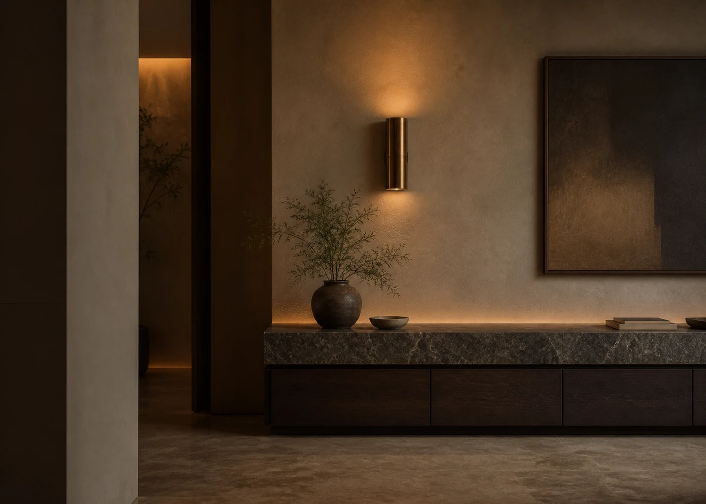 Warm brass wall sconce and concealed cove light washing lime plaster above a veined stone console.